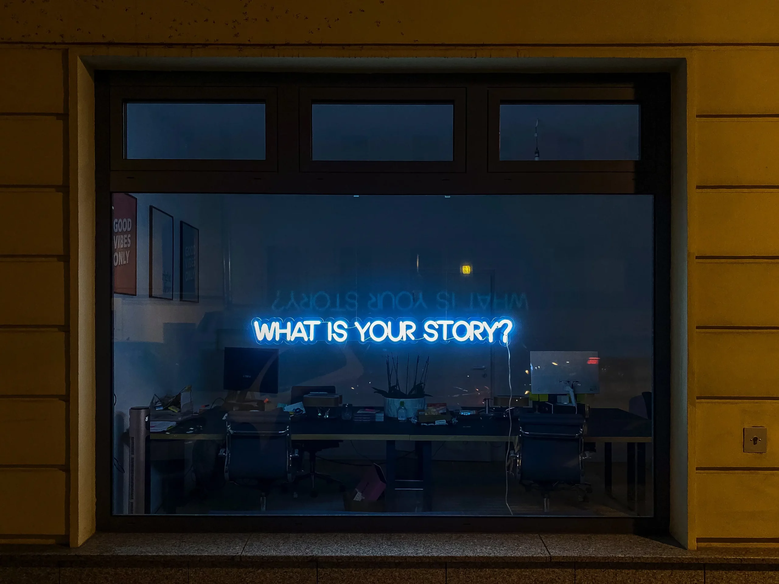 A window sign in neon blue that says: "what's your story?"